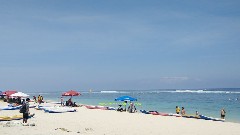 Visitors enjoying the sun and sea at Bali Shoreline, Bali, with colorful umbrellas and canoes.