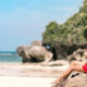 A girl sitting barefoot on the stone of Dreamland Beach Bali