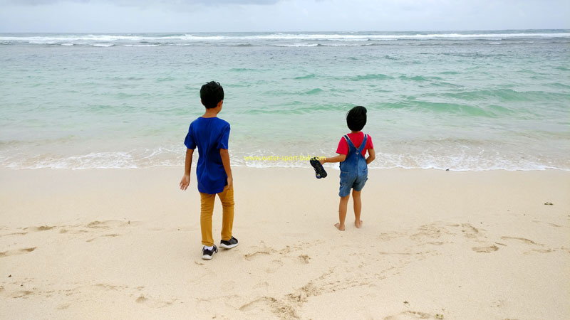 Two small children stand on the edge of Melasti Beach Ungasan, looking out at the blue ocean