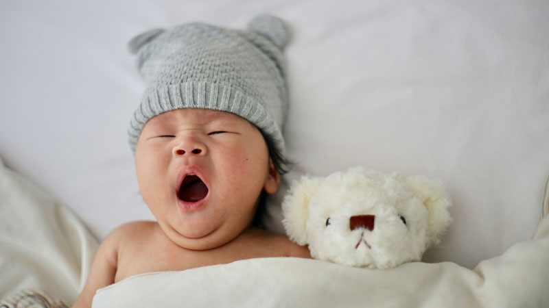 Baby yawns with teddy bear, ready for nap