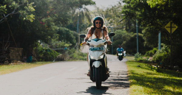 Traveler riding a motorbike on a sunlit Bali road towards Tanjung Benoa