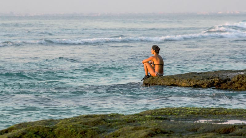 Visitors are sitting on the rocks at Suluban Beach Uluwatu, enjoying the view of the waves and blue sea.