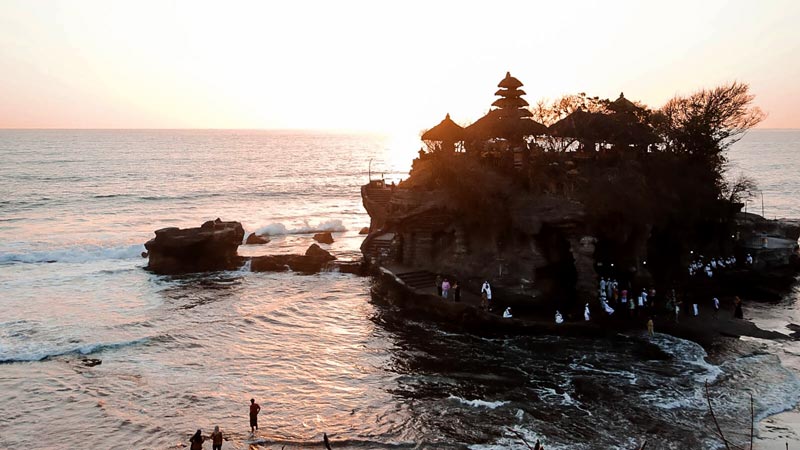 Tanah Lot Temple in Bali at sunset, with waves crashing all around