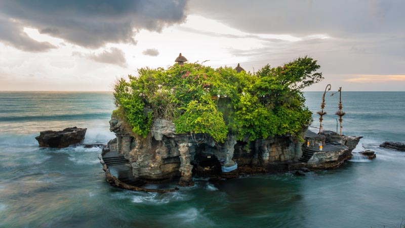 Tanah Lot Temple perched on a rock amidst sea waves at sunset. Best Places To Visit In Bali.