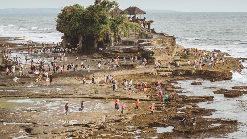 Crowds of visitors at the rocky beachfront of Tanah Lot Temple in Bali during low tide