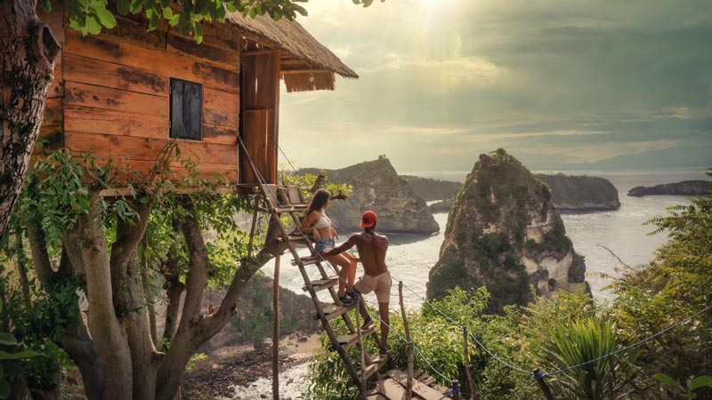 Couple enjoying a panoramic view from a treehouse overlooking the distinctive rock formations of Nusa Penida, Best Places To Visit In Bali.