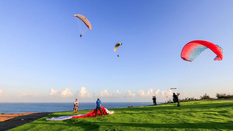 Tandem paragliding over the cliffs of Nusa Dua, with ocean backdrop. One of the best Bali water sports suitable for non-swimmers