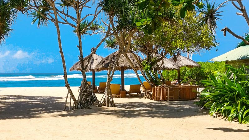 Nusa Dua Beach with huts and palm trees providing shade on the edge of the white sandy beach