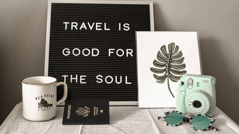 Inspirational travel message 'Travel is good for the soul' with passport and camera, essentials for exploring Bali.