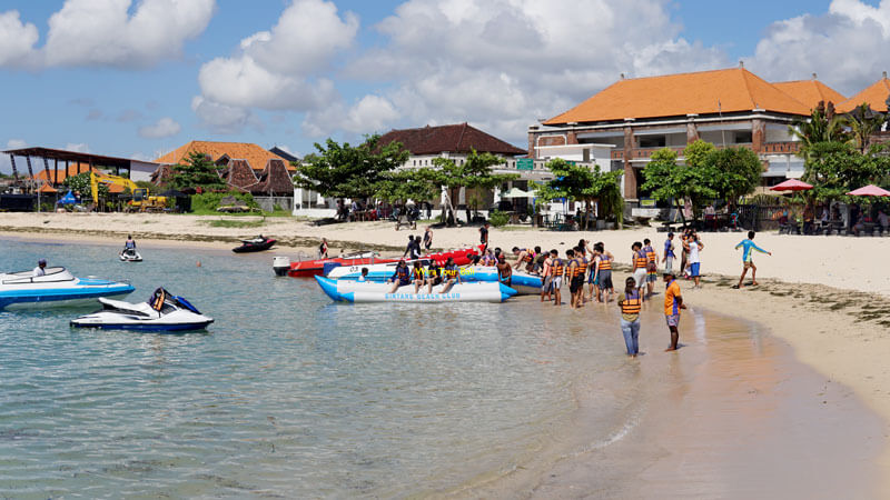 Visitors enjoying water sports at Tanjung Benoa Beach with boats and jet skis