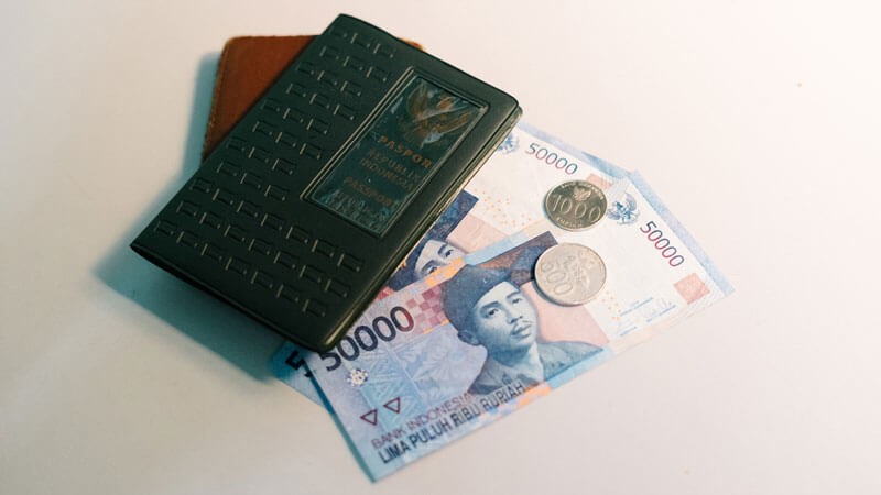 Indonesian Rupiah notes and coins with a passport wallet, representing travel expenses in Bali.