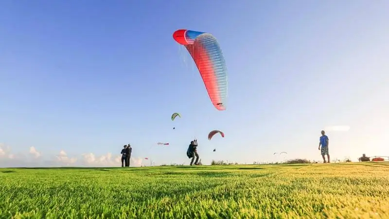 Pilot launching a paraglider from a grassy takeoff area with ocean view.