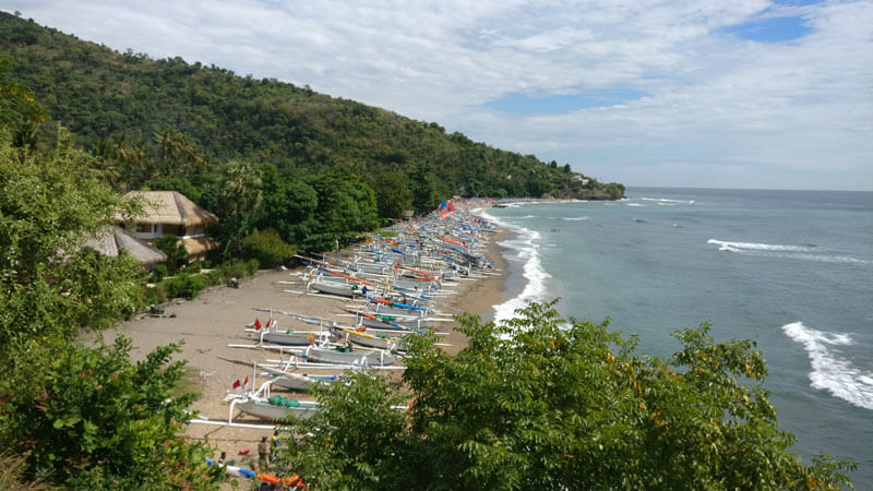 Traditional jukung outrigger boats lined up on Amed Beach with its distinctive black sand and lush greenery in the backdrop, East Bali.