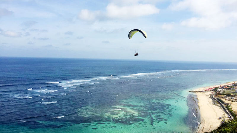 Paraglider soaring above the coastline Timbis Beach with clear blue skies.