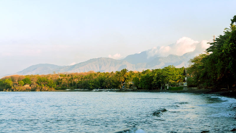 Scenic view of Tulamben Beach with Mount Agung in the background, highlighting the serene coastline and lush tropical greenery one of 5 Hidden Beaches in East Bali.