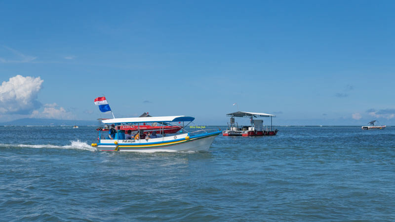 Glass-bottom boat cruising towards Turtle Island in Bali with clear skies above