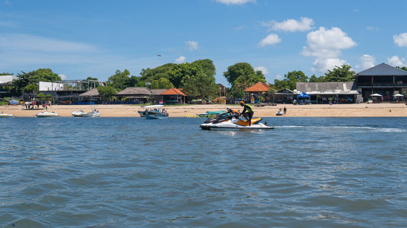 Jet ski enthusiasts gliding across the waters of Tanjung Benoa Beach with Bali shoreline in the background.