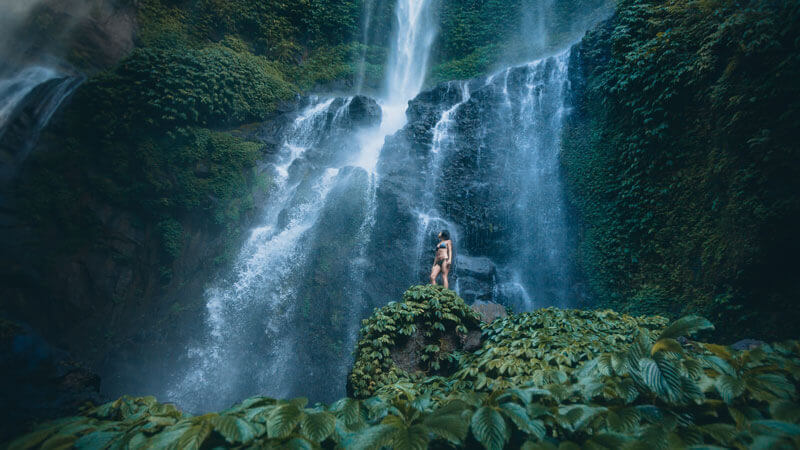 Hiker exploring dazzling Sekumpul Waterfall with rainbows, Unforgettable Activities in Bali for Young Adults