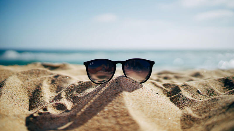 Sunglasses resting on the sun-kissed sands, with the gentle waves of the ocean in the background.