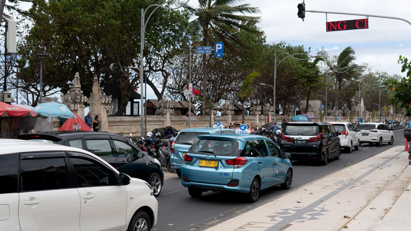 Busy street scene near Kuta Beach with cars and scooters lined up, Bali.