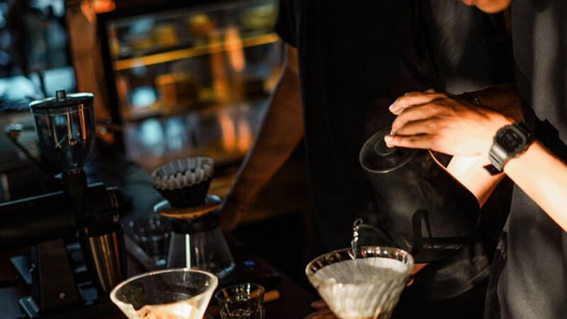 Barista precision-pouring water over coffee grounds in the ambient setting of 9/11 Cafe & Concept Store