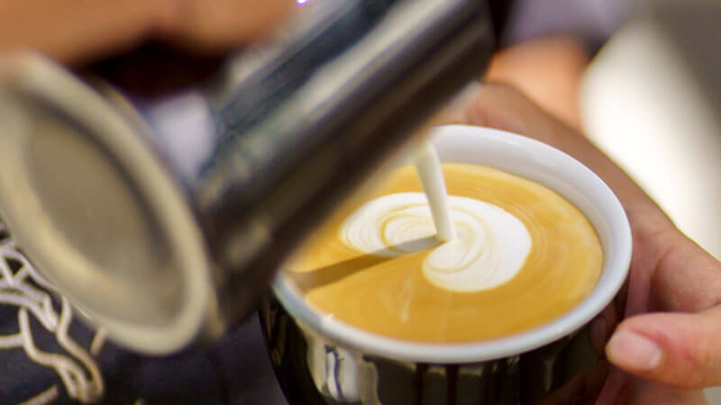 Barista pouring milk to create intricate latte art at Mitos Kopi Renon in Denpasar