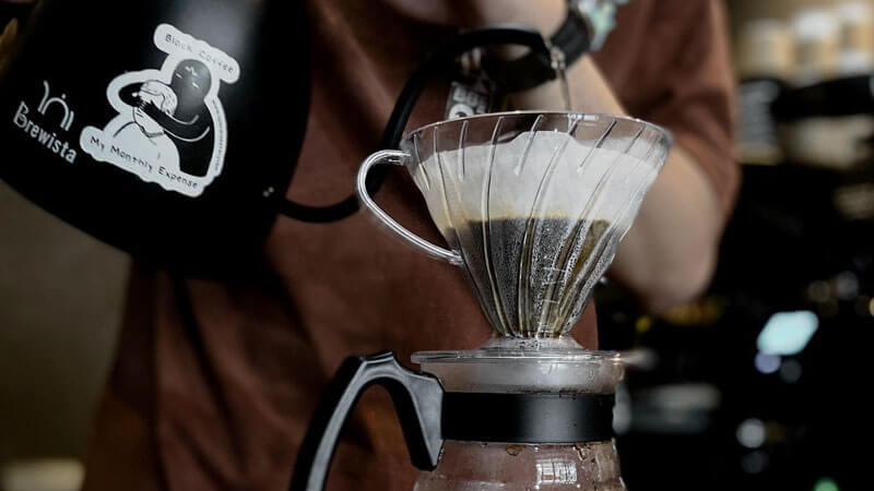 Close-up of a barista pouring water over coffee grounds using a Brewista kettle, highlighting the pour-over technique at Patmos Coffee