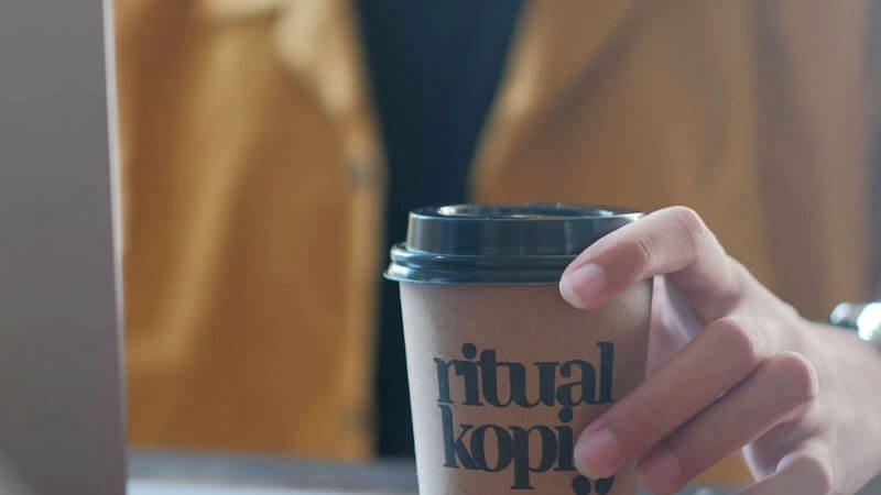 Close-up of a hand holding a takeaway coffee cup from Ritual Kopi Denpasar