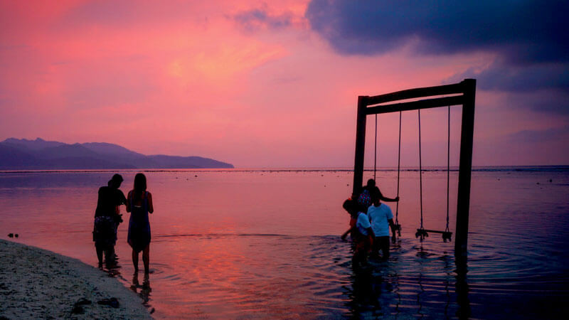 Travelers at Gili Trawangan beach during sunset with a silhouette of a swing.