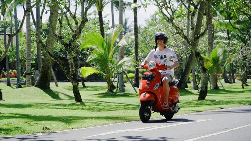 Tourist riding a scooter through Bali's scenic route.