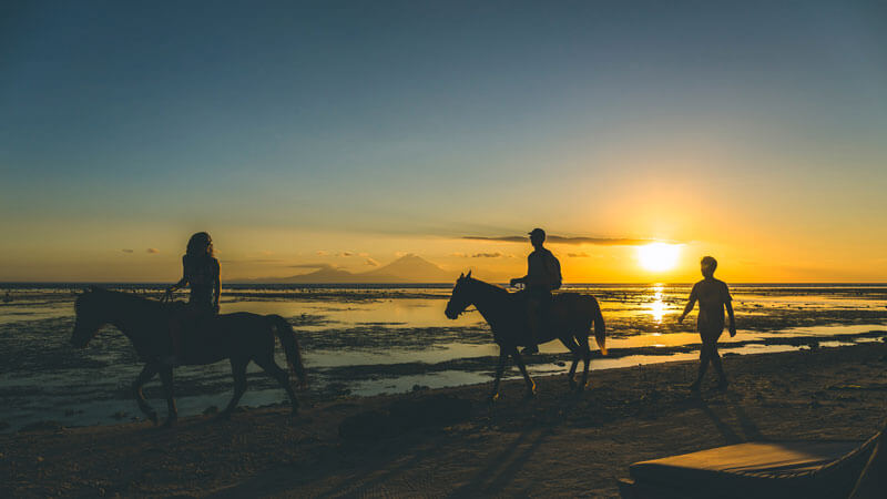 Horseback riding on Gili Trawangan beach at sunset with Mount Agung in the distance.