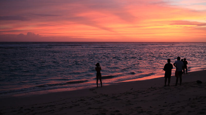 Breathtaking sunset at Gunung Payung Beach with silhouettes of people on shore