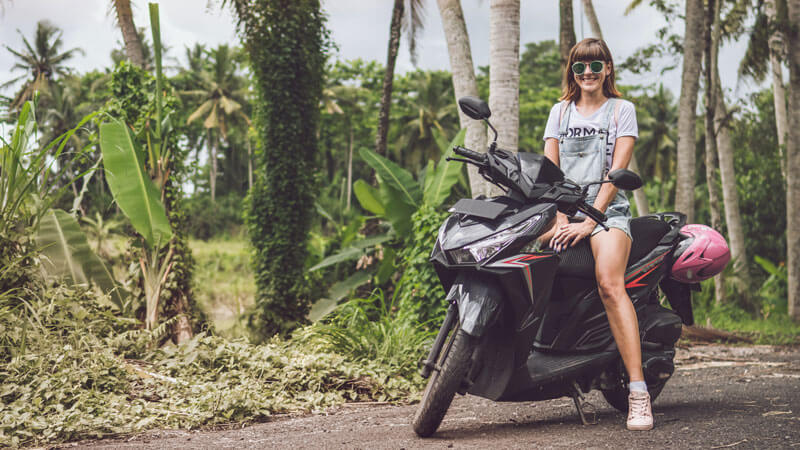 Tourist ready to explore Bali on a rented scooter amidst a lush tropical backdrop.