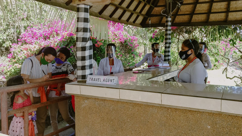 Family at travel agent desk in Uluwatu Temple discussing entrance fees and visit hours.