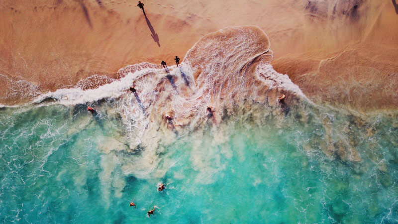 Aerial view of swimmers and turquoise waves at Bias Tugel Beach, East Bali