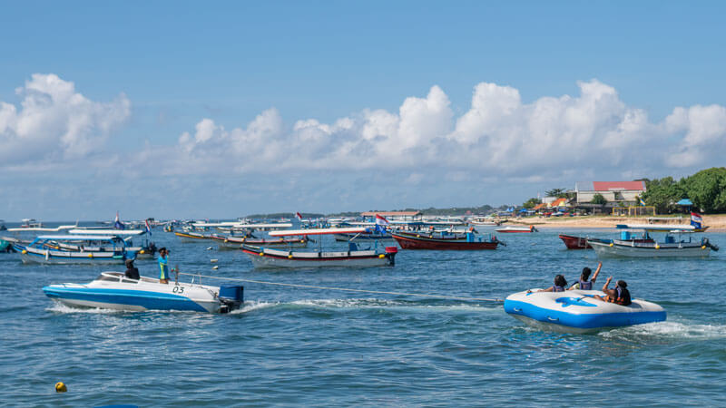 Tourists enjoying a Rolling Donut water ride in Tanjung Benoa with boats in the background