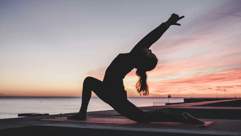 Woman practicing yoga on the beach at sunset in Bali