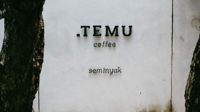 Titik Temu Coffee signage amidst trees in Seminyak, Bali.