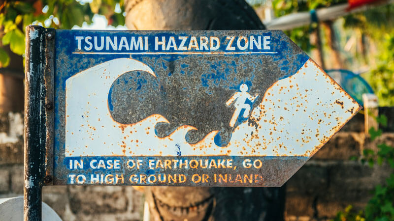 Aged tsunami hazard warning sign in East Bali, advising caution and swift evacuation to higher ground in case of an earthquake.