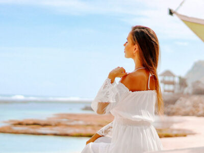 A serene view of a woman gazing at the ocean from a white sand beach in Bali, epitomizing the tranquil beauty of Bali's famous beaches.
