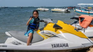 Child on jet ski at Bali beach showing peace sign