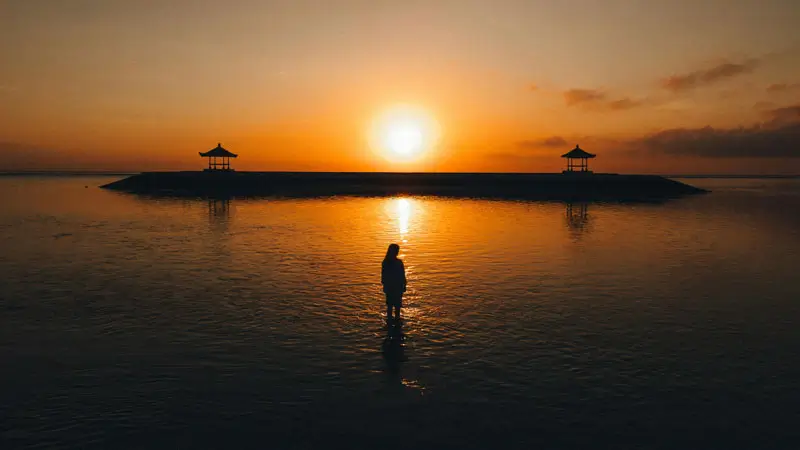 Sanur Beach sunrise with traditional Balinese gazebos and calm waters.