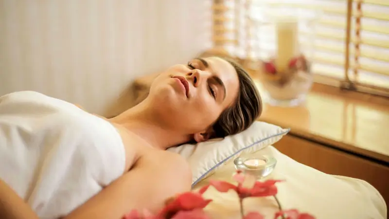 Woman relaxing during a spa treatment with flowers and candles in a serene setting.