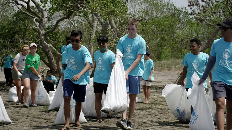 Ocean Cleanup Group participants carrying bags of recovered plastic during a beach cleanup.