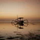 Sunrise at Sanur Beach Bali with a traditional jukung boat reflecting on the calm waters.