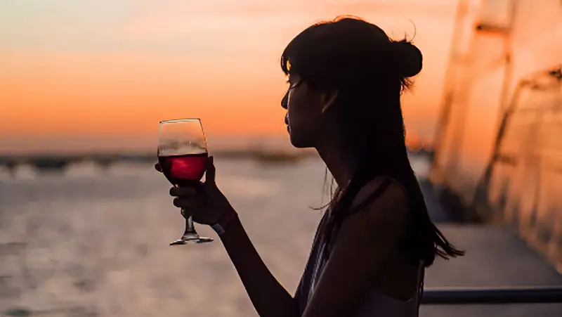 A woman enjoying a glass of wine while admiring the sunset on a Bali sunset cocktail cruise.
