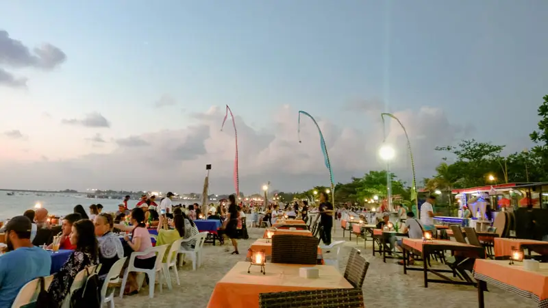 Crowded seafood restaurants set up along Jimbaran Beach Bali at dusk. © Wira Tour