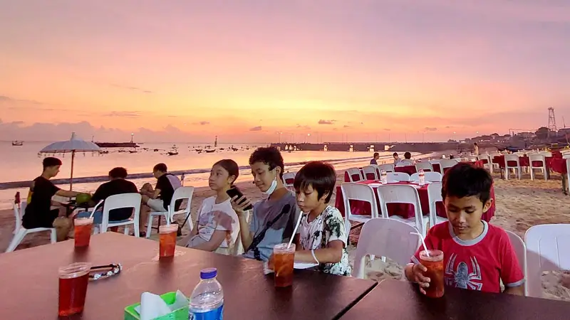 Family enjoying seafood dinner by the ocean at sunset on Bali beach © Wira Tour