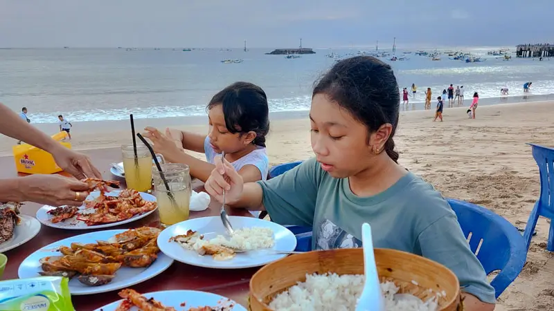 Kids eating grilled seafood dinner on the shoreline. © Wira Tour