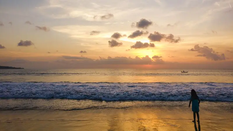 Woman walking along the shoreline of Jimbaran Beach Bali at sunset. © Wira Tour